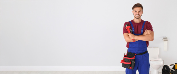 Young man with plumber wrench and toilet bowl on background, space for text. Banner design