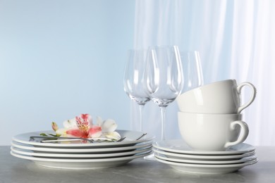 Photo of Glasses and clean dishware with flowers on grey marble table