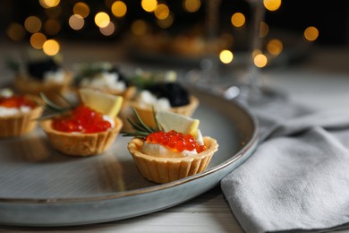 Photo of Delicious tartlets with red and black caviar served on white wooden table, closeup. Space for text