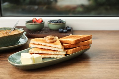Photo of Tasty toasts and different toppings on wooden table at window