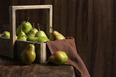 Basket with ripe pears on wooden table. Space for text