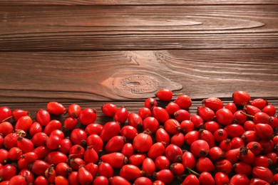 Photo of Fresh ripe rosehip berries on wooden table. Space for text