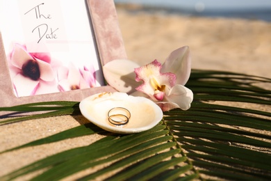 Shell with gold rings, wedding invitation and beautiful flower on sandy beach