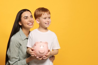 Mother and her son with ceramic piggy bank on orange background, space for text