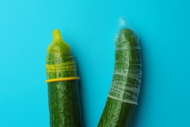 Cucumbers with condoms on light blue background, flat lay. Safe sex concept