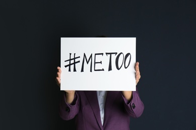 Woman holding paper with text "#METOO" on dark background. Problem of sexual harassment at work