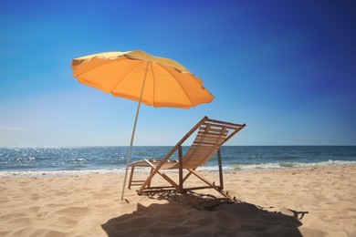 Orange beach umbrella and deck chair on sandy seashore