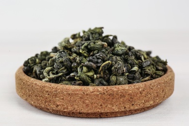 Dried green tea leaves in cork bowl on white table, closeup