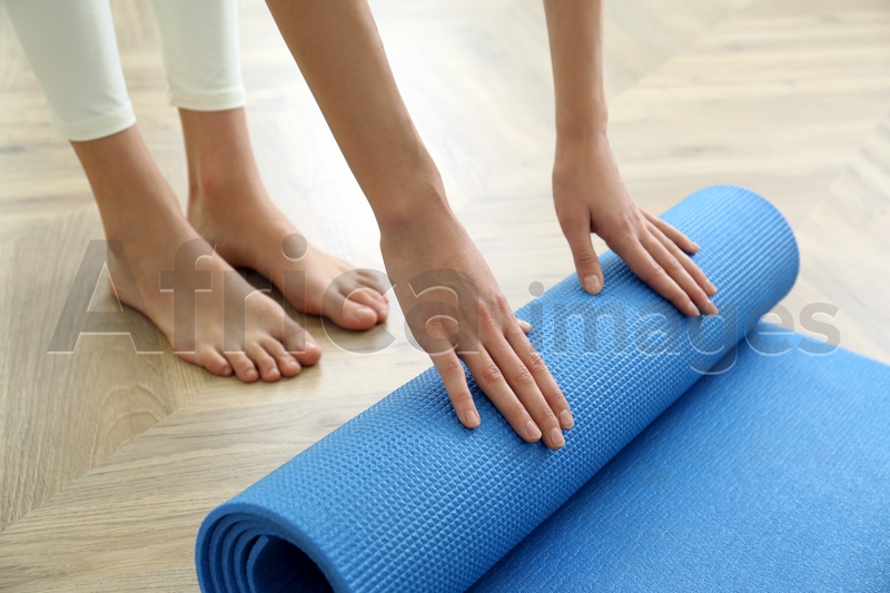 Woman rolling blue yoga mat indoors, closeup