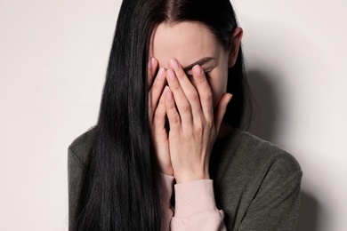 Upset young woman crying against light background