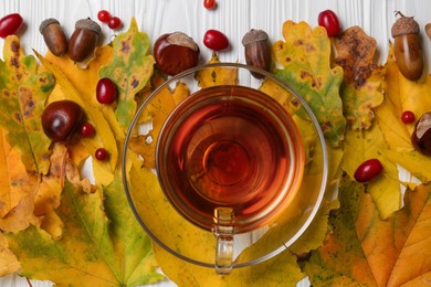 Photo of Different autumn leaves, acorns, chestnuts, red berries and cup of tasty tea on table, flat lay