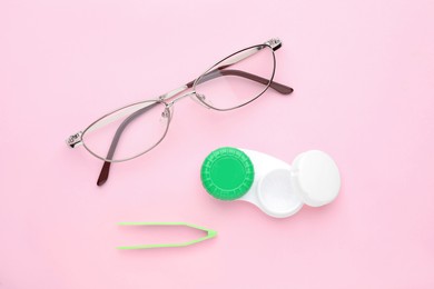 Case with contact lenses, tweezers and glasses on pink background, flat lay