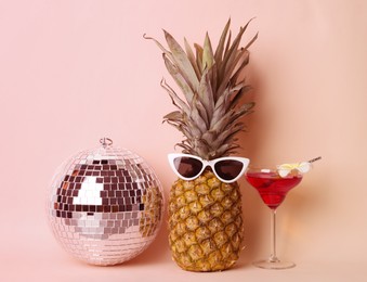 Funny pineapple with sunglasses, cocktail and disco ball on pink background. Summer party
