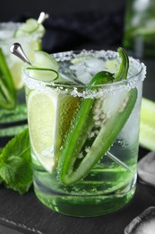 Spicy cocktail with jalapeno, cucumber and lime on black table, closeup
