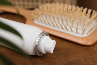 Dry shampoo spray and hairbrush on wooden table, closeup