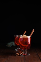 Glasses with red mulled wine on wooden table against dark background. Space for text