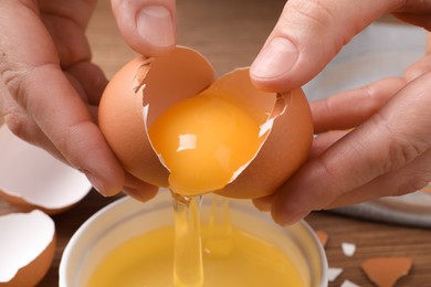 Woman separating egg yolk from white over bowl at table, closeup