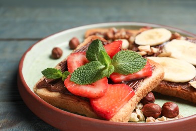 Tasty toasts with chocolate spread, nuts, strawberries, banana and mint served on wooden table, closeup