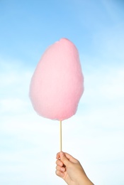 Woman holding sweet pink cotton candy on blue sky background, closeup view