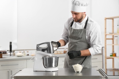 Photo of Male pastry chef preparing dough in mixer at kitchen table