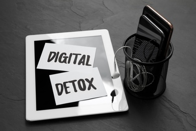 Paper notes with phrase DIGITAL DETOX and different gadgets on black stone table