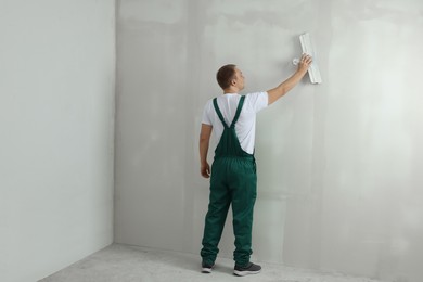 Photo of Professional worker plastering wall with putty knife indoors