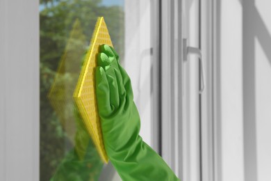 Woman cleaning window glass with sponge cloth indoors, closeup