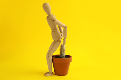 Wooden human figure and cactus on yellow background. Hemorrhoid problems