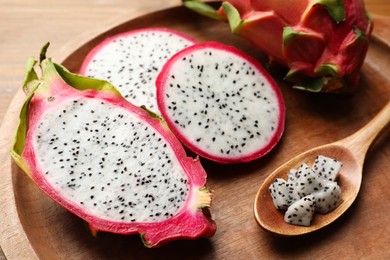 Wooden plate of delicious cut and whole white pitahaya fruits with spoon on table, closeup