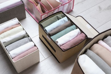 Different cases and organizer with folded clothes on white wooden background. Vertical storage