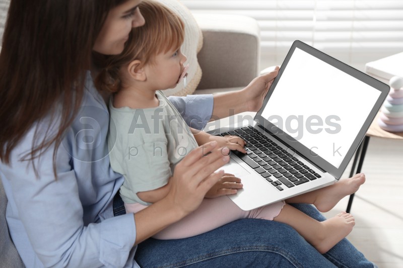 Photo of Mother and daughter sitting with laptop on sofa at home. Pediatrician online consultation