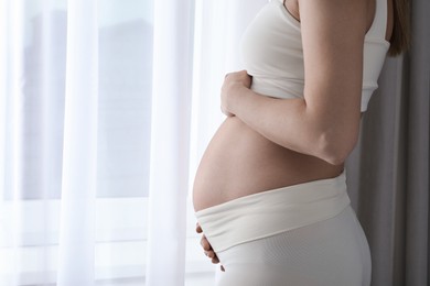 Pregnant woman near window at home, closeup. Space for text
