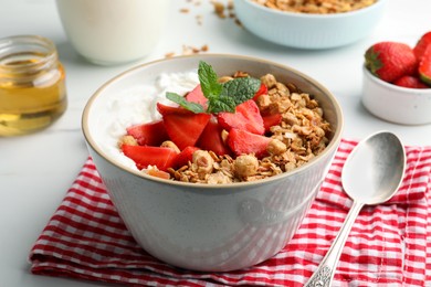 Photo of Bowl with tasty granola and strawberries served on white table, closeup. Healthy meal