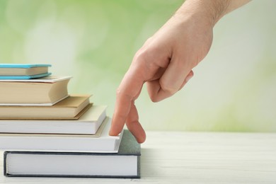 Man climbing up stairs of books with fingers on white wooden table against blurred background, closeup
