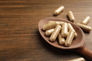 Dietary supplement capsules with spoon on wooden table, closeup. Space for text