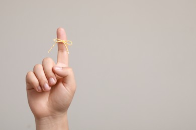 Photo of Man showing index finger with tied bow as reminder on light grey background, closeup. Space for text