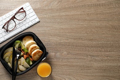 Photo of Container of tasty food, keyboard, cutlery and glasses on wooden table, flat lay with space for text. Business lunch