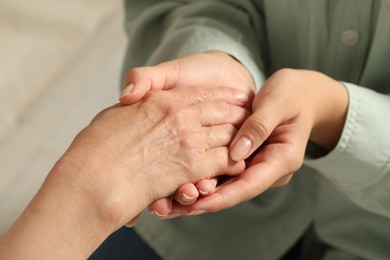 Photo of Young and elderly women holding hands indoors, closeup