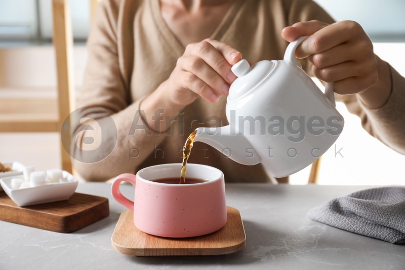 Woman pouring tea into ceramic cup at table, closeup