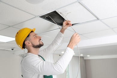 Electrician in uniform repairing ceiling wiring indoors
