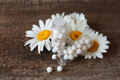Bottles with homeopathic remedy and flowers on wooden table