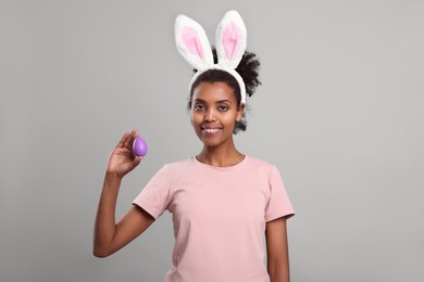 Photo of Happy African American woman in bunny ears headband with Easter egg on gray background