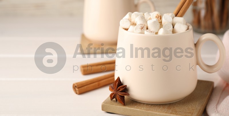 Cup of hot drink with marshmallows and aromatic cinnamon on white table. Space for text