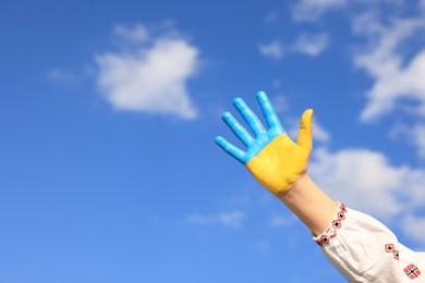 Little girl with hand painted in Ukrainian flag colors against blue sky, closeup and space for text. Love Ukraine concept