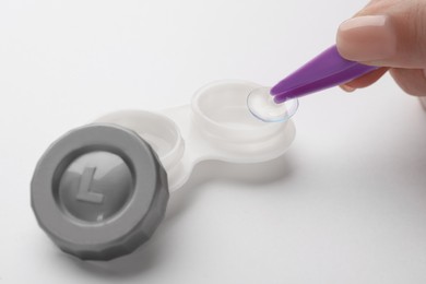 Photo of Woman taking contact lens from case with tweezers on white background, closeup