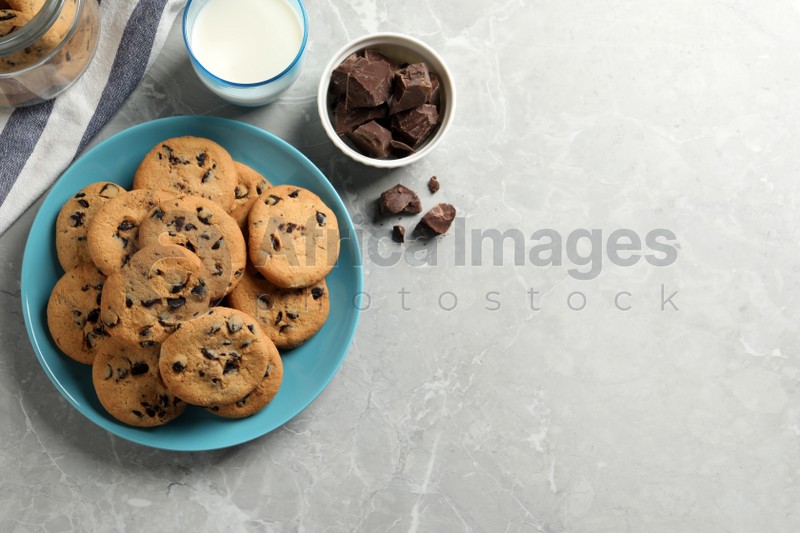 Delicious chocolate chip cookies and glass of milk on grey marble table, flat lay. Space for text