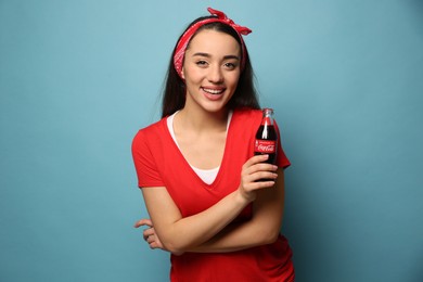MYKOLAIV, UKRAINE - JANUARY 27, 2021: Young woman holding bottle of Coca-Cola on light blue background