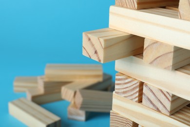 Jenga tower made of wooden blocks on light blue background, closeup. Space for text