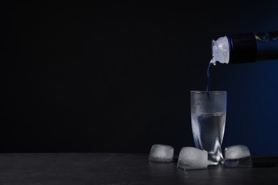 Pouring vodka from bottle into shot glass on black table against dark background. Space for text
