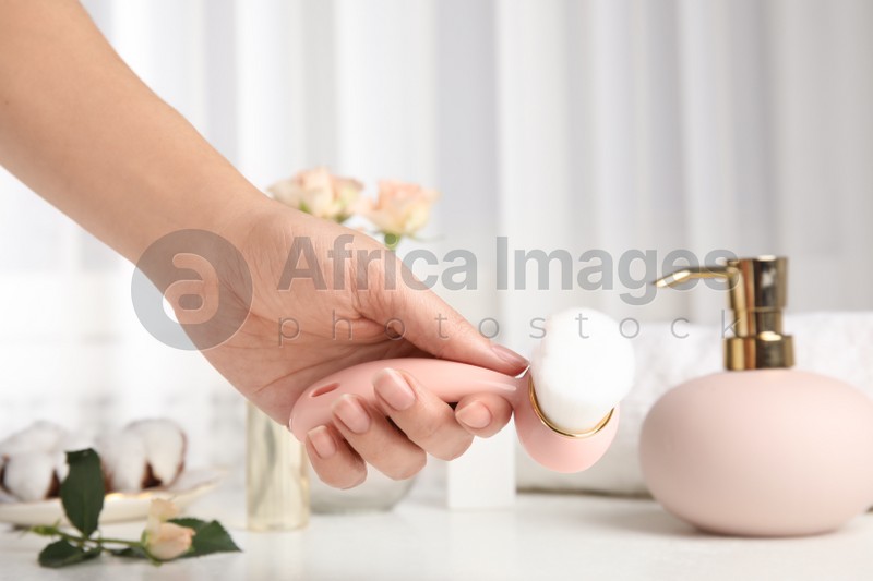 Photo of Woman holding face cleansing brush over white table, closeup. Cosmetic accessory